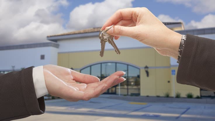 Female hand giving keys to palm up male hand in front of business.